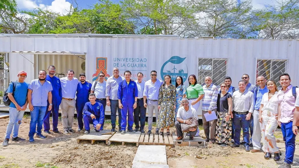 Grupo de personas mayores posando en un espacio con tierra. Detrás tienen un contenedor que dice “Universidad de La Guajira”.