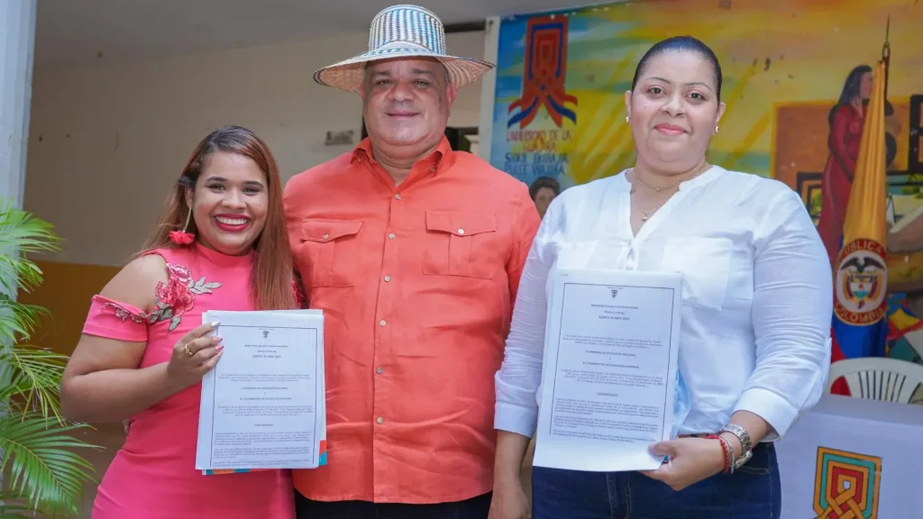 Dos mujeres sosteniendo unos documentos, con un hombre en el centro que es de contextura gruesa, alto y tiene un sombrero Wayuú.
