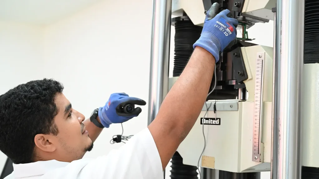 Un hombre con bata y guantes está en un laboratorio de Ingeniería Mecánica.