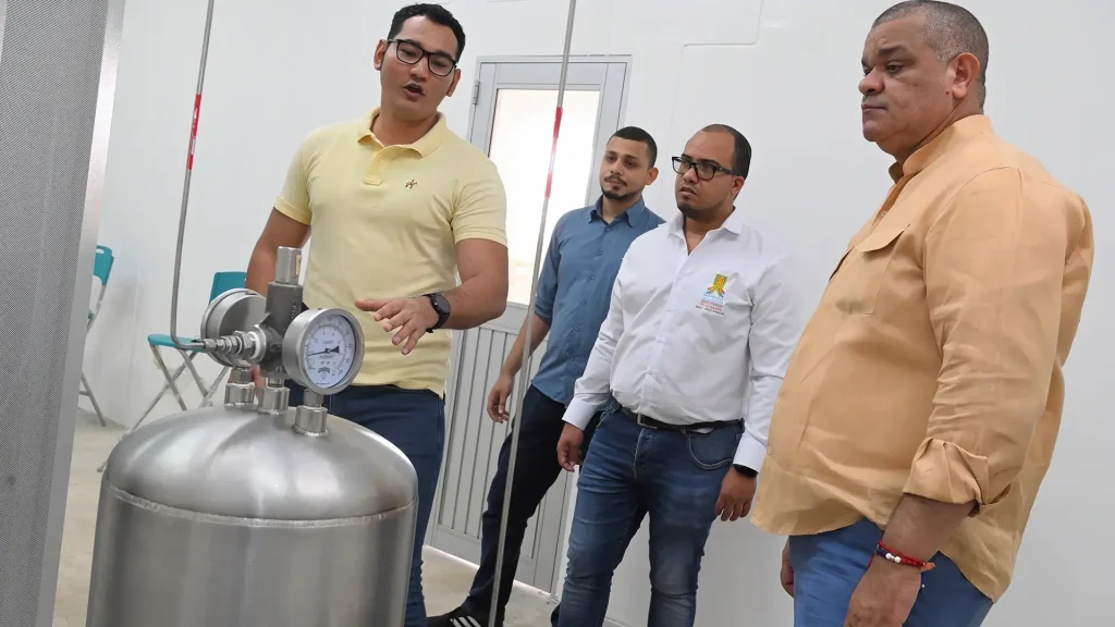 Cuatro hombres en un espacio cerrado; uno de ellos se encuentra explicando y señalando un elemento de ingeniería.