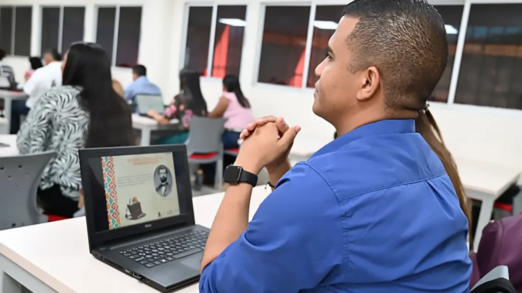 Un estudiante con camisa azul mirando una presentación en su laptop.