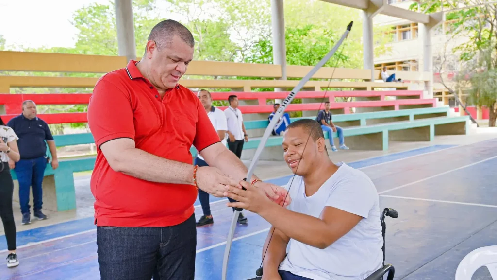 Un hombre adulto y un jóven en silla de rueda recibiendo un equipo deportivo