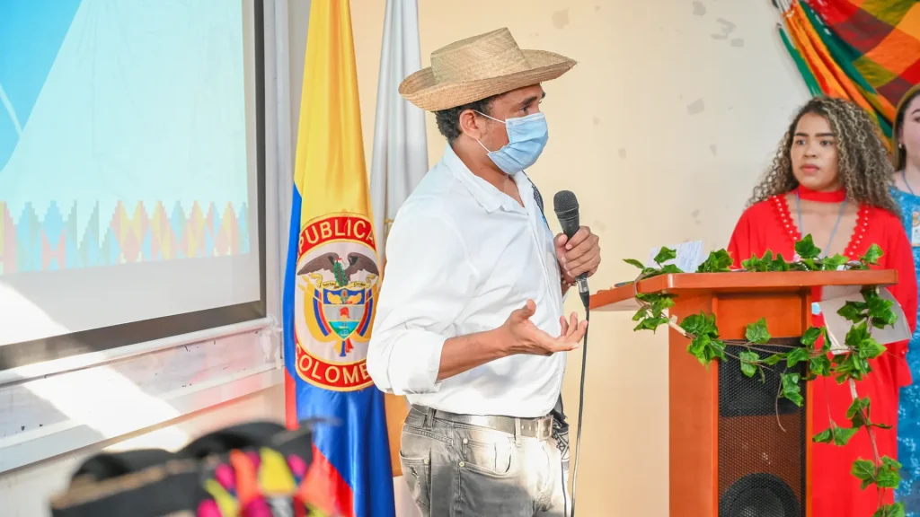 Hombre adulto habla por un micrófono frente a un público.