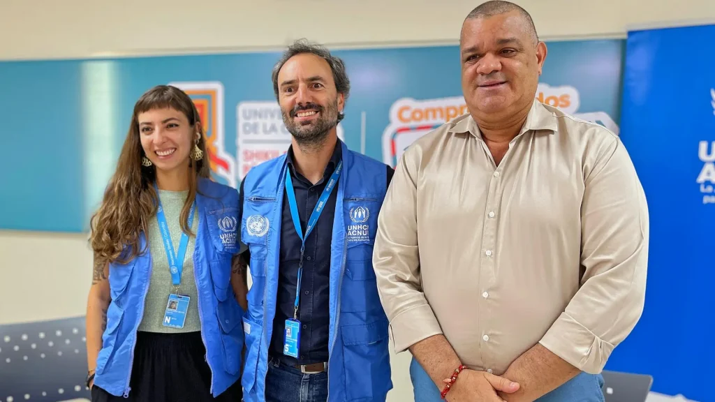 Tres personas de pie en un aula universitaria celebrando la firma de una alianza institucional.