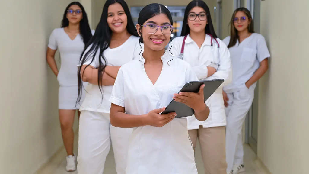 Un grupo de cinco estudiantes de medicina con batas blancas posando en un pasillo.