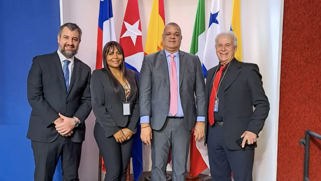Cuatro hombres y una mujer adulta posan para una foto, frente a las banderas de varios países. 
