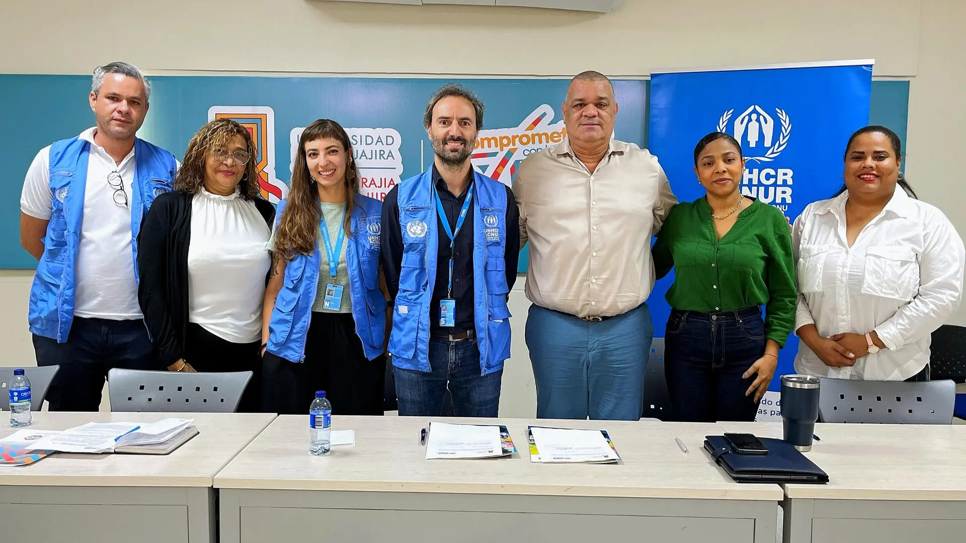Siete personas de pie en un aula universitaria, celebrando la firma de una alianza estratégica.