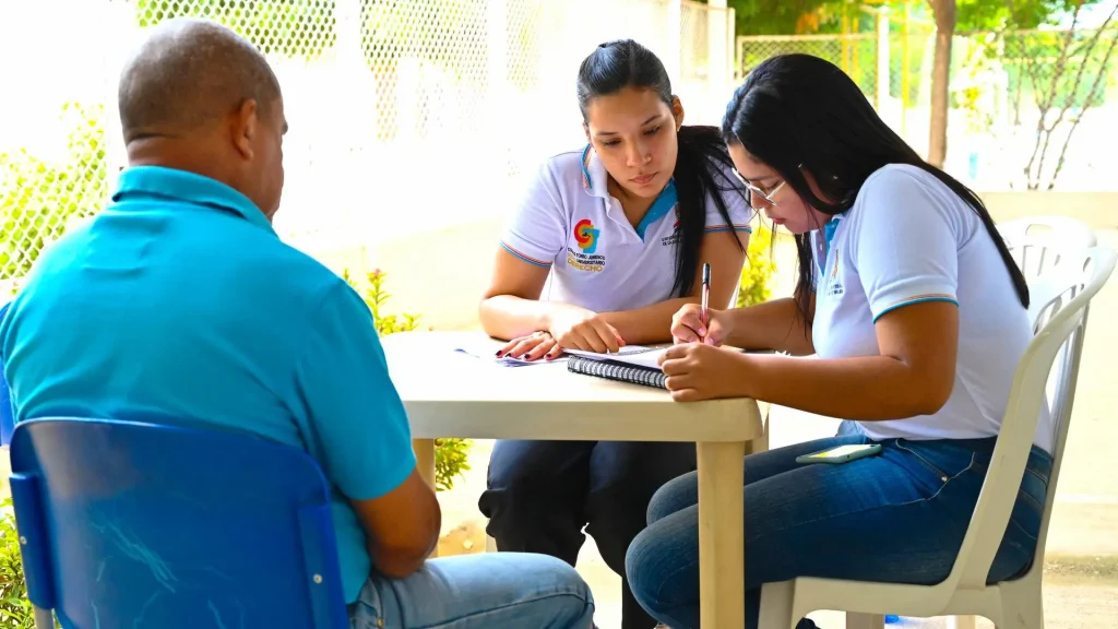 Tres personas adultas en una mesa escribiendo, dos mujeres y un hombre

