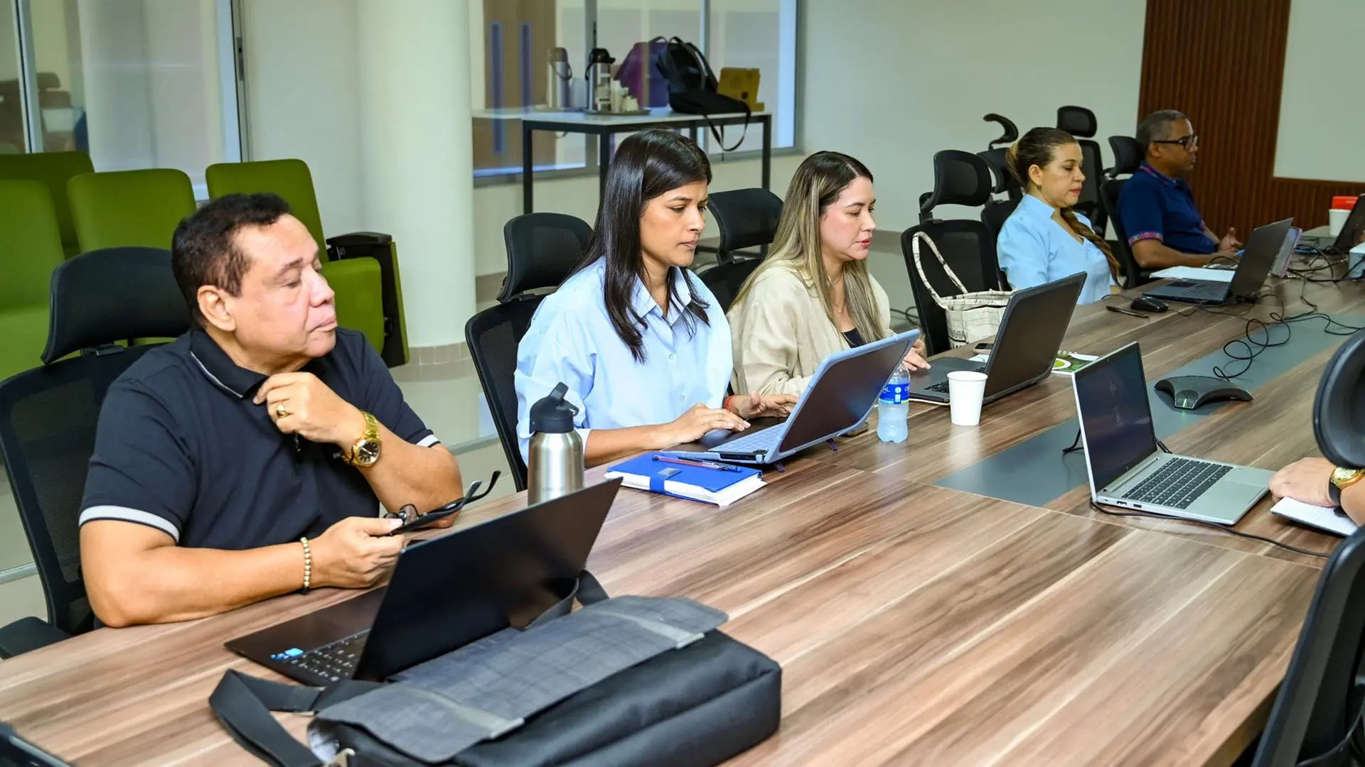 Un grupo de directivos y representantes institucionales posan sentados en un escritorio, frente a un computador portátil.