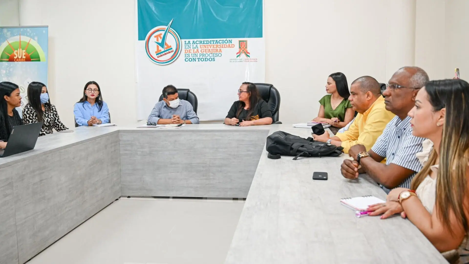 Un grupo de personas participa en una mesa de trabajo en la que se desarrolla una jornada de auditoría. Los asistentes, ubicados alrededor de la mesa, escuchan y toman nota de las intervenciones, mostrando atención e interés en el encuentro.