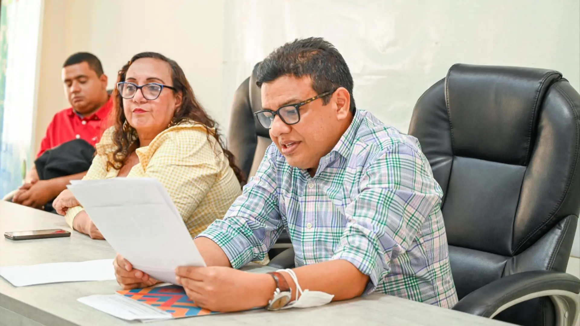 Durante una reunión de auditoría, uno de los participantes lee en voz alta un documento mientras otros asistentes siguen el desarrollo de la actividad. La escena refleja un espacio de diálogo y revisión colectiva.