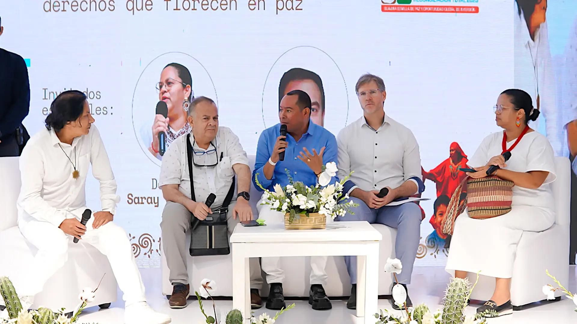 Panel de discusión del Foro “Semillas de Paz”, con cinco panelistas sentados en el escenario conversando sobre los derechos y la reconciliación. Al fondo se proyecta la temática “Caminos de esperanza: derechos que florecen en paz”.