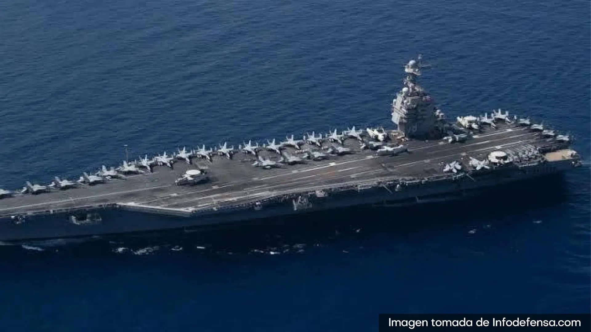 Portaaviones navegando en mar abierto con varios aviones de combate alineados sobre su cubierta de vuelo.