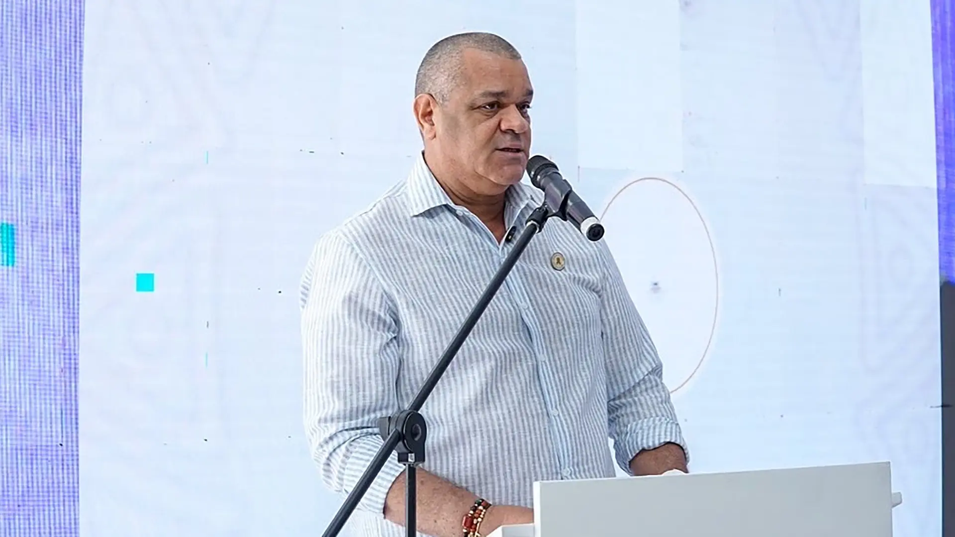 Carlos Arturo Robles Julio, rector de Uniguajira, hablando frente a un micrófono durante su intervención en el Foro “Semillas de Paz”. Viste camisa de rayas y se encuentra frente a un podio con fondo blanco.