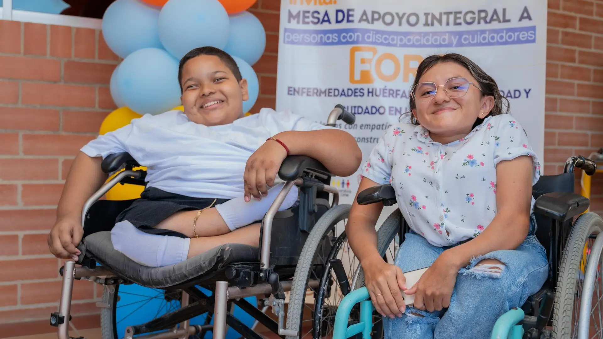 Dos participantes jóvenes en silla de ruedas sonríen durante un encuentro sobre discapacidad y enfermedades huérfanas.