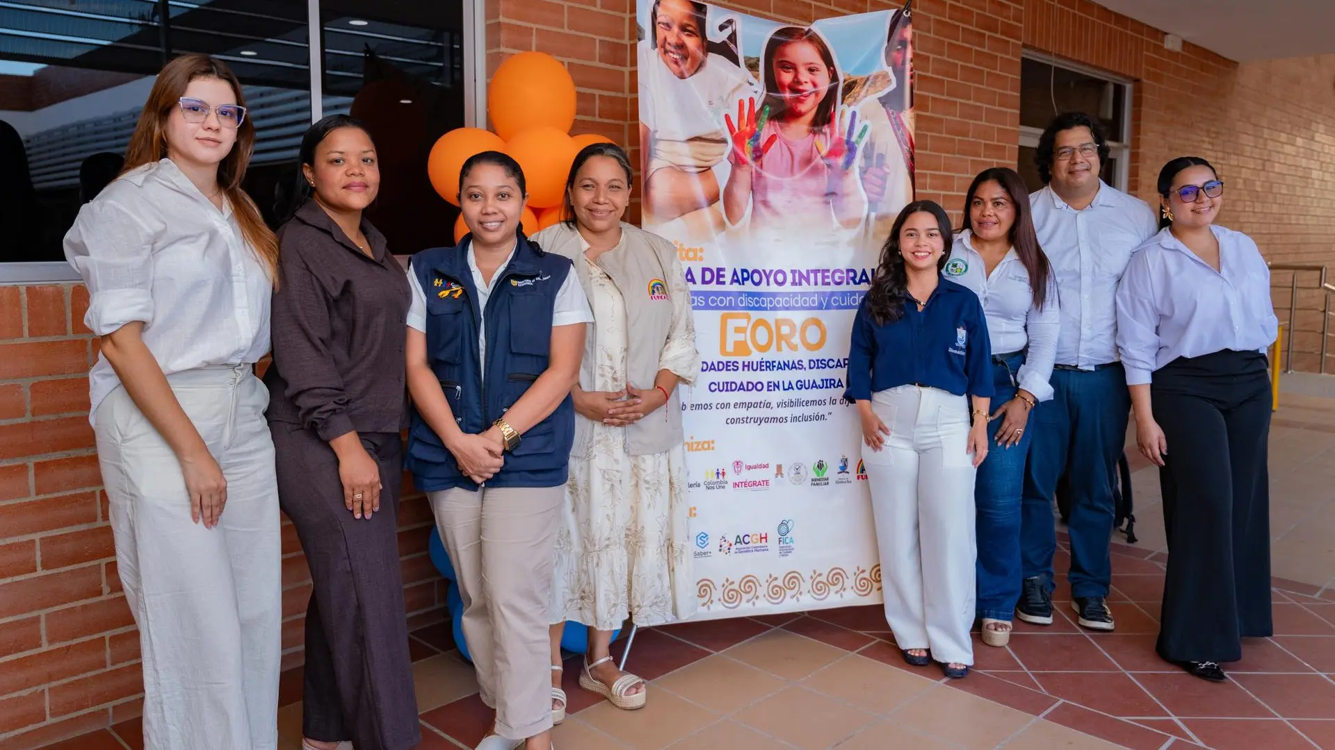 Grupo de profesionales y representantes institucionales posan juntos frente a un cartel del foro sobre apoyo integral a personas con discapacidad en La Guajira.