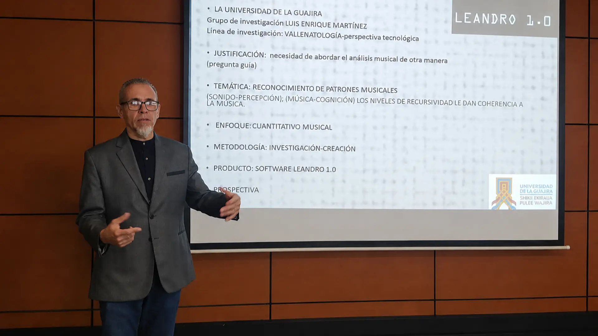 Docente durante la presentación del software Leandro 1.0, frente a una pantalla que muestra información sobre el proyecto de investigación y su metodología en el campo de la música vallenata.