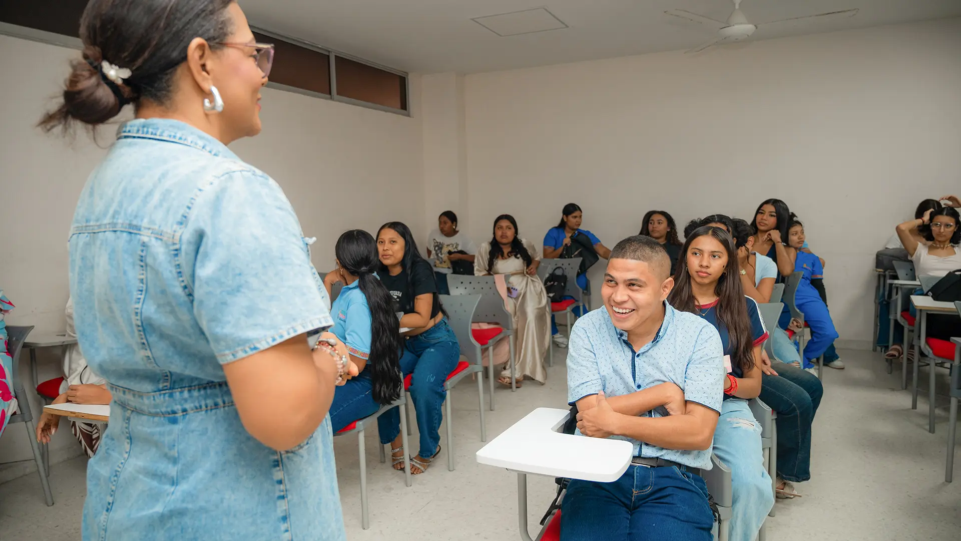 Rafael David Niño Atencio, estudiante de Trabajo Social de la Universidad de La Guajira, sonríe mientras participa en una actividad en el salón de clases, acompañado por una integrante de la comunidad universitaria y sus compañeros.